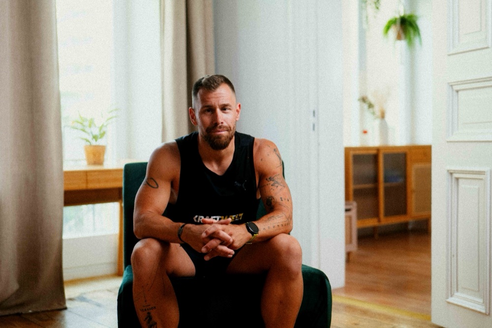 Coach Laurenz im Kraftwelt-Shirt, sitzend im Wohnzimmer-Setting